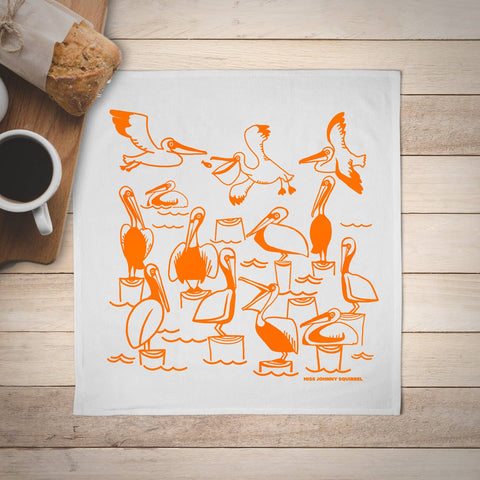 White towel with orange pelican designs on a wooden surface with a cup of coffee.