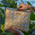 Hand holding a patterned pouch with a brand name against a green leafy background