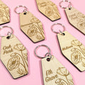 Wooden keychains with engraved text and floral designs on a pink background