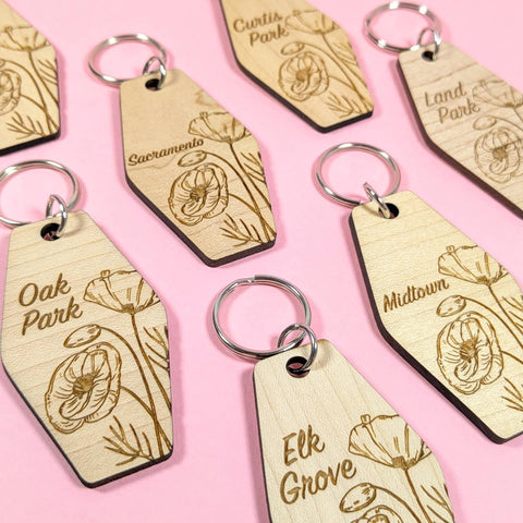 Wooden keychains with engraved text and floral designs on a pink background