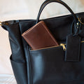 Black leather handbag with a brown wallet inside, on a light background