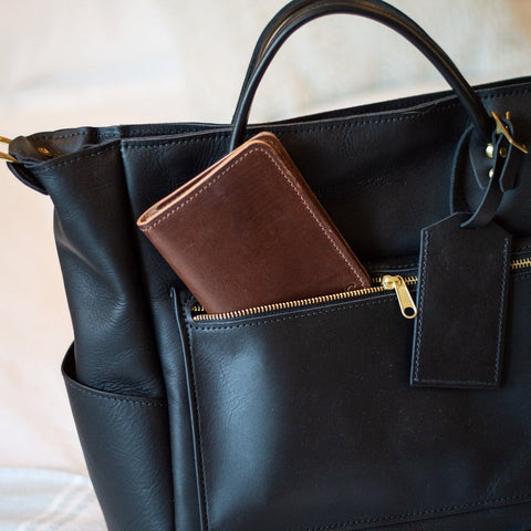 Black leather handbag with a brown wallet inside, on a light background