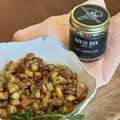 Hand holding a jar of North Fork Char Co. seasoning over a bowl of roasted potatoes.