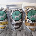 Three packages of dog treats from 'The Barkery' on a wooden surface.