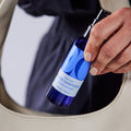 Hand holding a blue hand sanitizer bottle over a beige bag.
