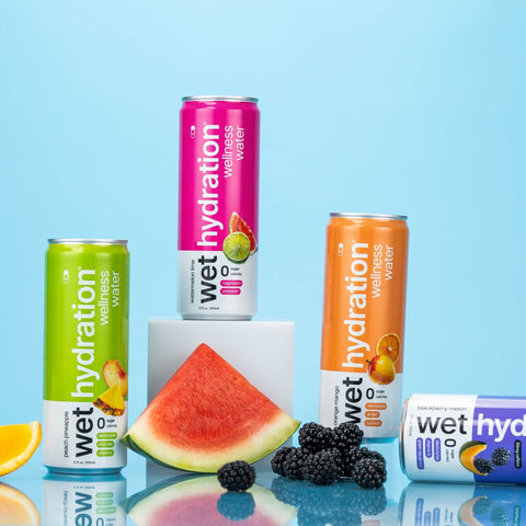 Assorted cans of Wet Hydration wellness water with fruits on a reflective surface and blue background