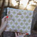 Hand holding a pouch with bee pattern against a blurred natural background