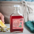 Bottle of Land & Local rose cardamom meyer lemon syrup on a table with a lemon and green leaves.