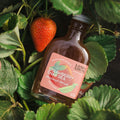 Bottle of strawberry snap pea syrup with a strawberry on a bed of green leaves