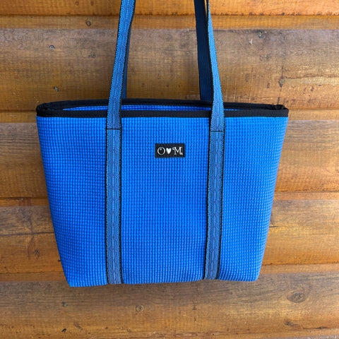 Blue tote bag with black trim against a wooden background