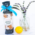 Packaged lavender and meyer lemon caramels with a blue ribbon, lemon, and vase of lavender on a white background.