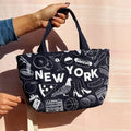 Two tote bags with 'New York' design held by a person against a light pink background