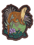 Embroidered patch of a beaver in a natural setting with leaves and flowers.
