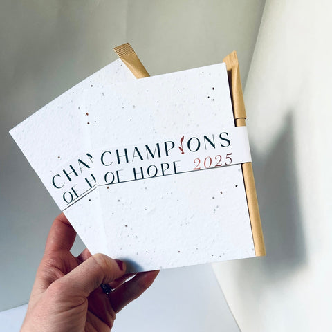 Hand holding a white calendar with 'Champions of Hope 2025' text on a light background