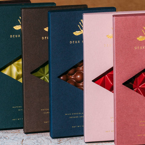 Five chocolate boxes with different colors and designs on a textured surface.