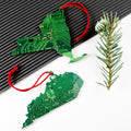 Two green circuit board Christmas ornaments shaped like dragons on a white background with a pine branch.