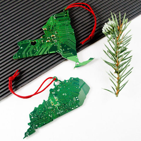 Two green circuit board Christmas ornaments shaped like dragons on a white background with a pine branch.