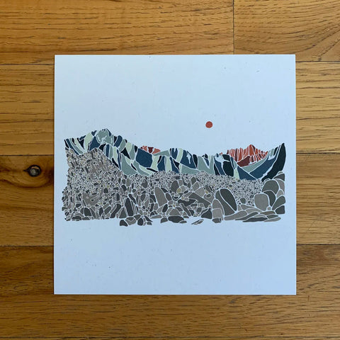 Art print of a mountain landscape on a white sheet of paper, placed on a wooden surface.