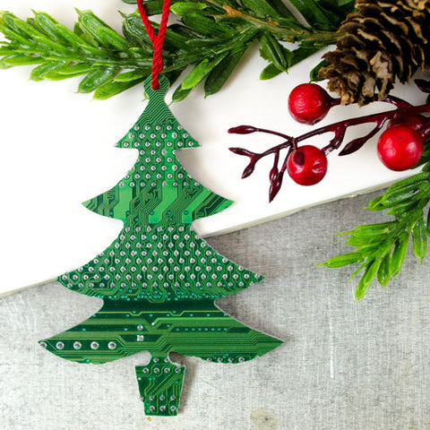 Christmas tree-shaped ornament made from a green circuit board on a white surface with greenery and berries.