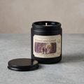 Candle in a black tin with a label featuring 'Hansel and Gretel' on a gray surface.