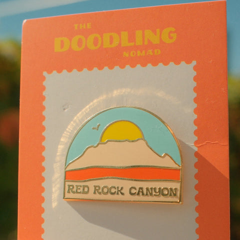 Enamel pin of Red Rock Canyon in packaging with 'The Doodling Nomad' branding.