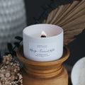 White candle with a label on a wooden holder against a dark background