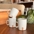 Two ceramic mugs stacked on a wooden table with a blurred indoor setting.