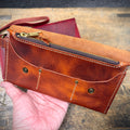 Brown leather clutch with gold zipper held by a hand on a wooden surface
