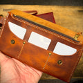 Brown leather wallet with gold accents held by a hand on a wooden surface