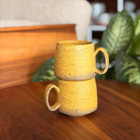Two yellow ceramic mugs stacked on a wooden surface with a blurred indoor background.