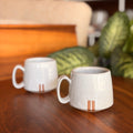 Two ceramic mugs on a wooden surface with a blurred indoor background
