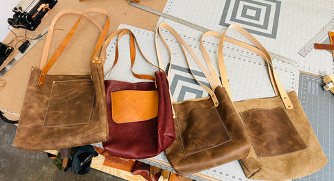 Four brown leather handbags on a cutting mat with tools in the background