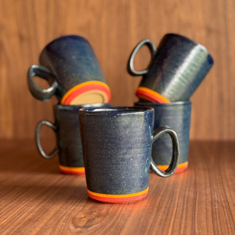 Set of black ceramic mugs with orange rims on a wooden surface