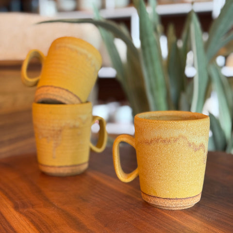 Three yellow ceramic mugs on a wooden surface with a blurred indoor background