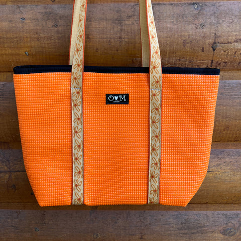 Orange tote bag with checkered pattern and wooden handle against a wooden background