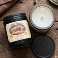 Candle labeled 'Rodeo Nights' with a black lid on a wooden surface.