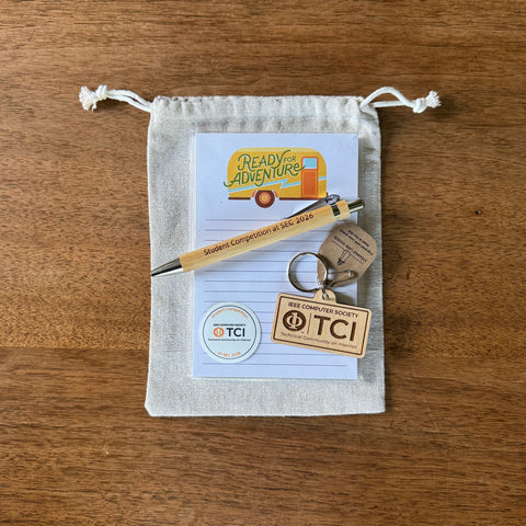 A small beige drawstring pouch on a wooden surface containing a lined notepad with a yellow camper graphic, a wooden pen, a metal key ring, and two TCI branded wooden key tags.
