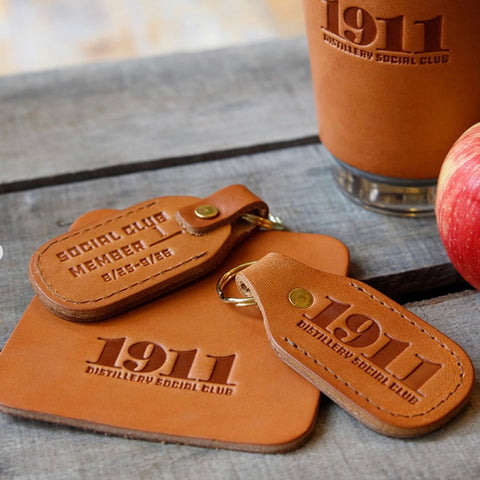 Brown leather keychain and tag with '1911 Distillery Social Club' branding on a wooden surface.