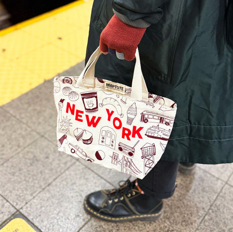 Person holding a tote bag with 'New York' text and graphics on a subway platform.