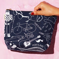 Navy blue pouch with white illustrations held by a hand on a pink background