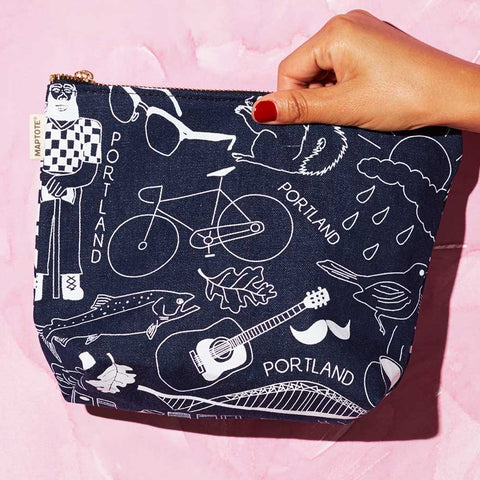 Navy blue pouch with white illustrations held by a hand on a pink background