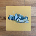 Art print of mountains on a yellow background, placed on a wooden surface