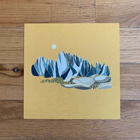 Art print of mountains on a yellow background, placed on a wooden surface