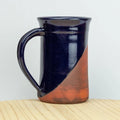 Two-toned ceramic mug with dark blue top and red bottom on a light wooden surface.