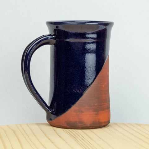 Two-toned ceramic mug with dark blue top and red bottom on a light wooden surface.