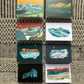 Set of small postcards with mountain and nature-themed illustrations arranged on a textured surface.