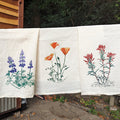 Three towels with floral designs hanging on a line outdoors.