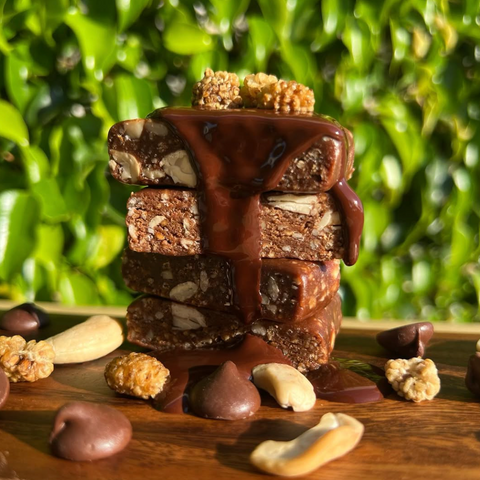 Stack of chocolate-dipped bars with nuts on a wooden surface against a green leafy background