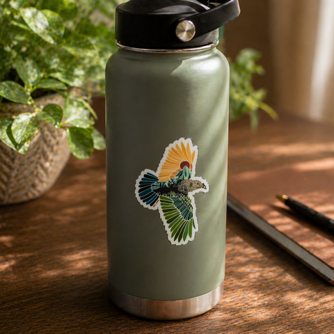 Green insulated bottle with a bird design on a wooden surface with a plant and notebook in the background