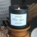 Black candle with a label on a wooden stand, surrounded by decorative elements.